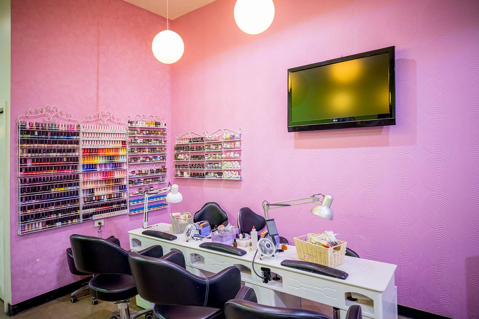 The pink manicure zone with wire-rack polish shelves, marble tables and wall TV