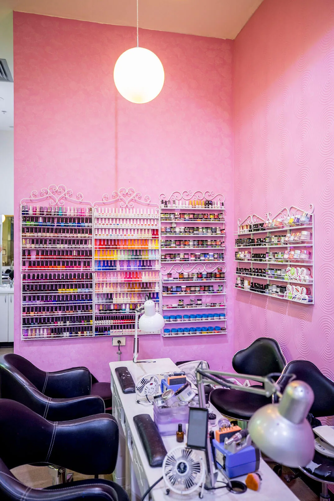 Tall pink wall lined with vintage-scroll wire racks of nail polish bottles