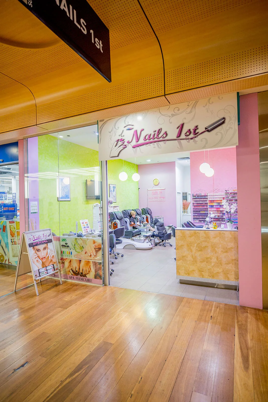 Nails 1st shopfront — cream signboard with cursive wordmark and the colourful interior beyond